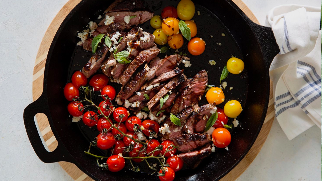 A cast iron skillet filled with sliced steak and tomatoes.