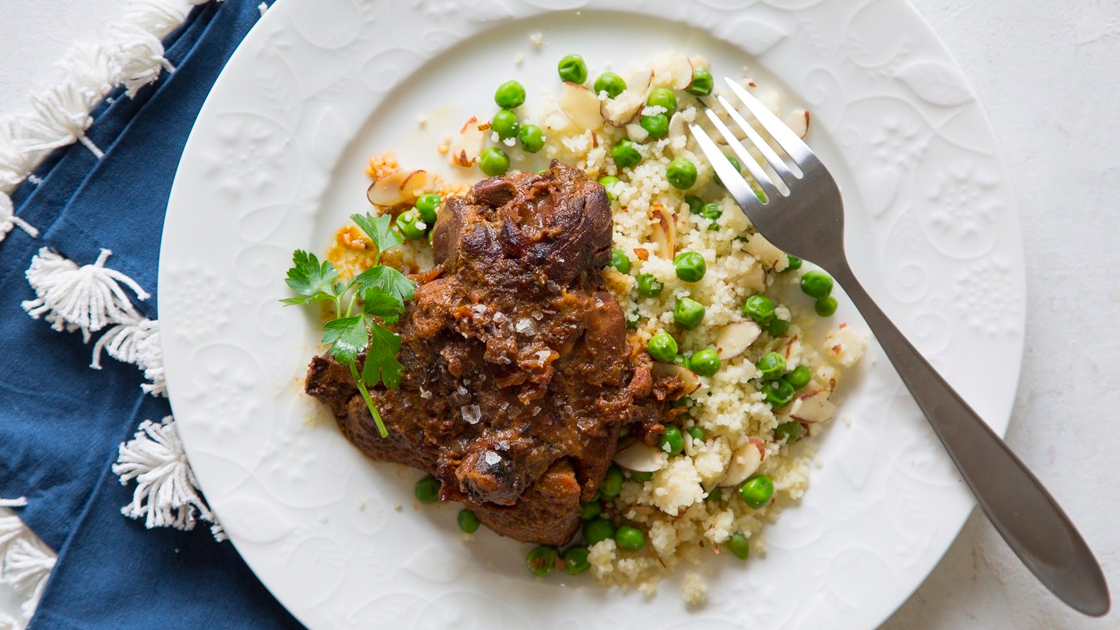 Spiced chicken with couscous and peas on a white plate on top of a blue napkin with tassels.