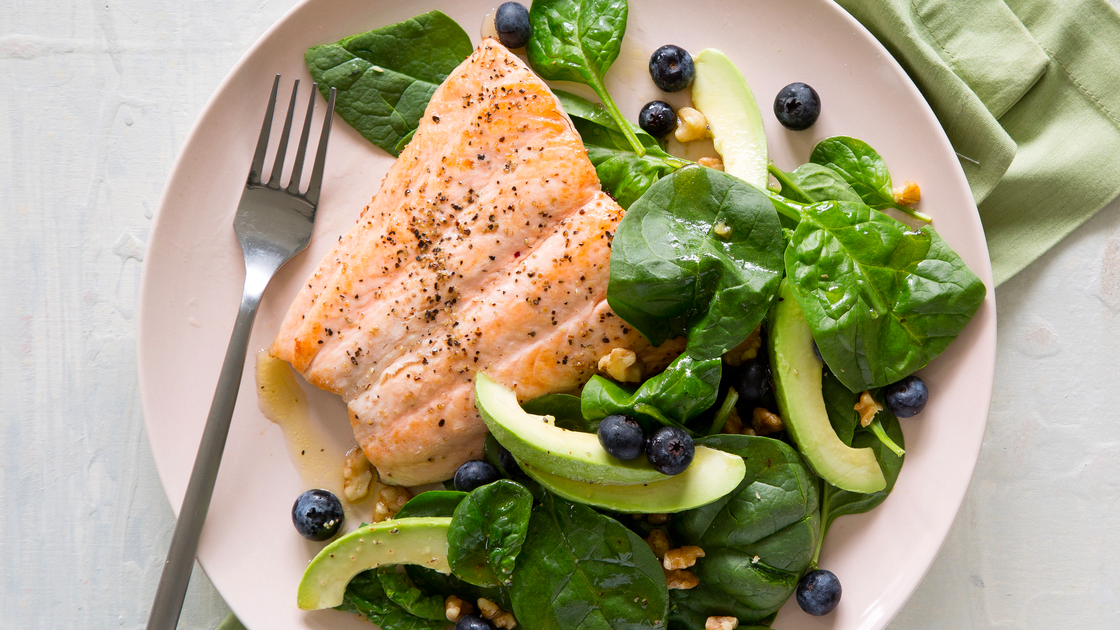 A plate with a large salmon fillet and spinach, avocado and blueberry salad.