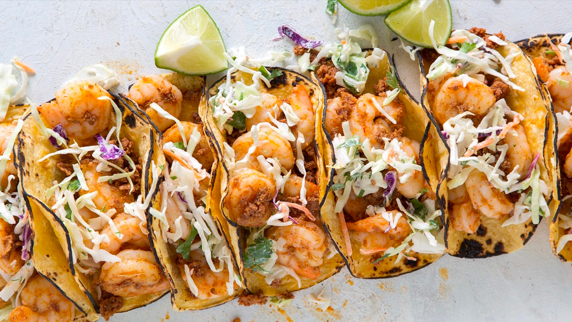 A row of shrimp tacos with lime wedges.