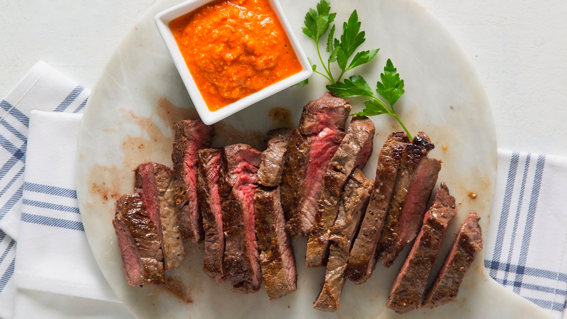 A plate with sliced steak with a side of romesco sauce.
