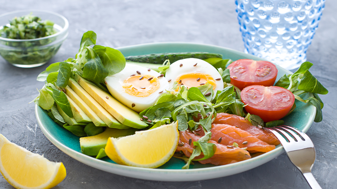 A healthy lunch plate featuring sliced avocado, hard-boiled egg, tomatoes, and smoked salmon.