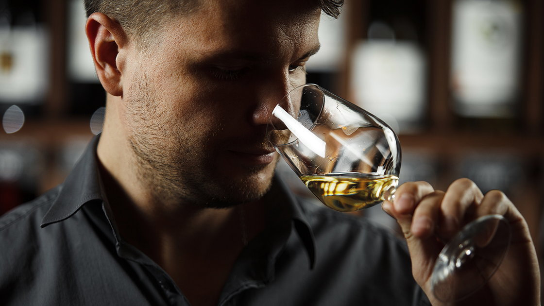 A man sniffing a glass of white wine.